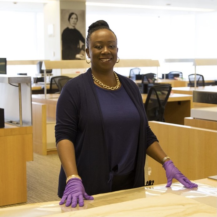 Woman standing behind desk wearing purple gloves