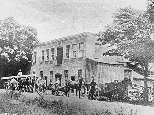 Black and white photo of two story building with horses and buggies in front.