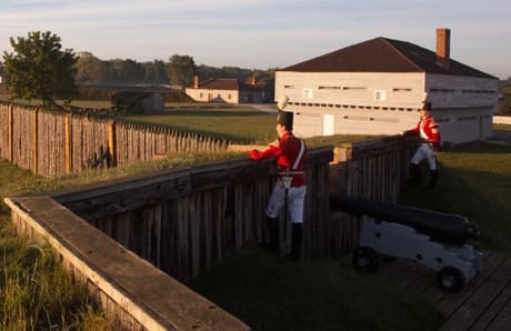 Two men in full British war of 1812 dress looks over a wall at dusk at Fort George