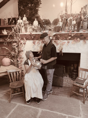 A man and woman in pioneer costumes sitting in front of a fireplace