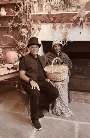 A couple in pioneer costumes sitting in front of a fireplace