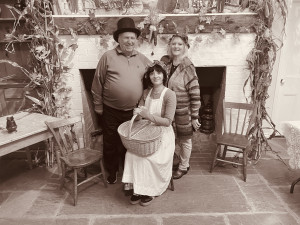 Three people in pioneer costumes sitting in front of a fireplace