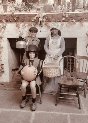 Three children in pioneer costumes sitting in front of a fireplace