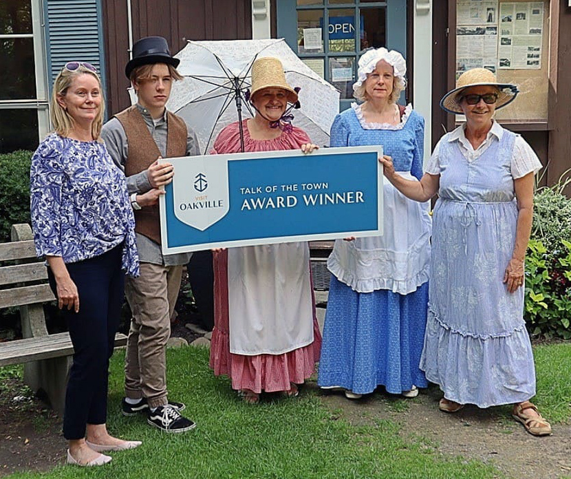 group of volunteers standing in front of OHS cottage on grass holding sign that reads talk of the town award winner