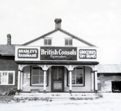 an old one story building with signs that read bradleys hardware and groceries soft drinks and an advertisement for British consols