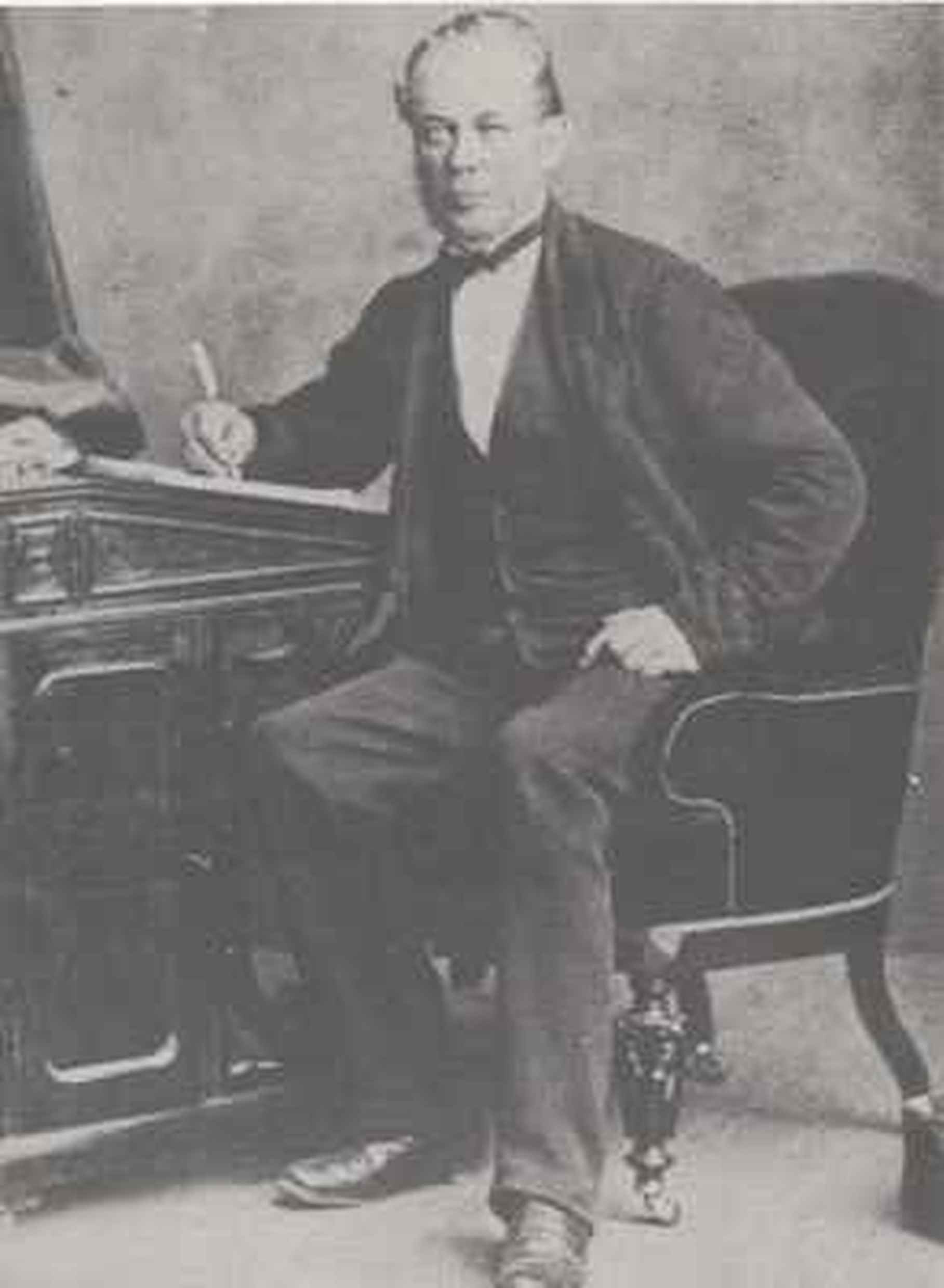 Black and White photo of GK Chisholm sitting at a desk facing camera