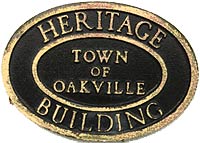 Old oval black plaque that reads Town of Oakville heritage plaque in gold letters