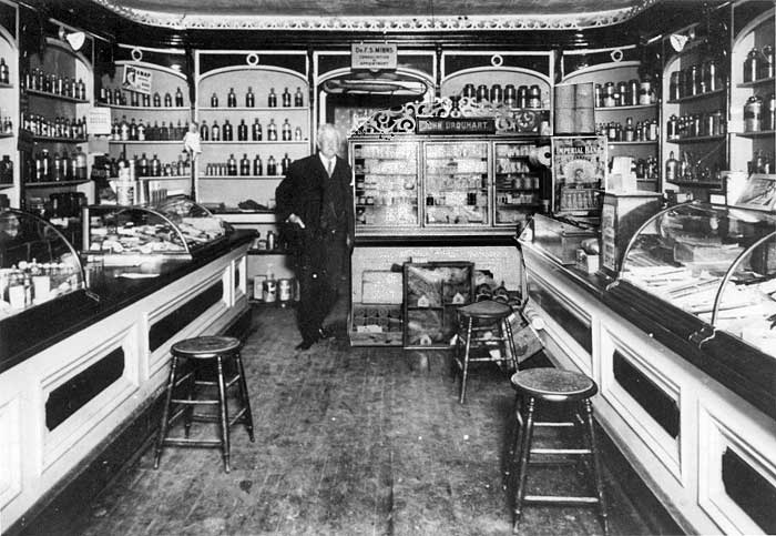 vintage photo of man standing in his pharmacy surrounded by bottles